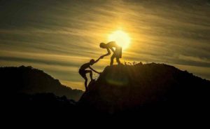 A boy helping another climb atop a mountain