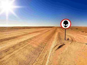 A desert road with a sign on the side containing the face of an alien